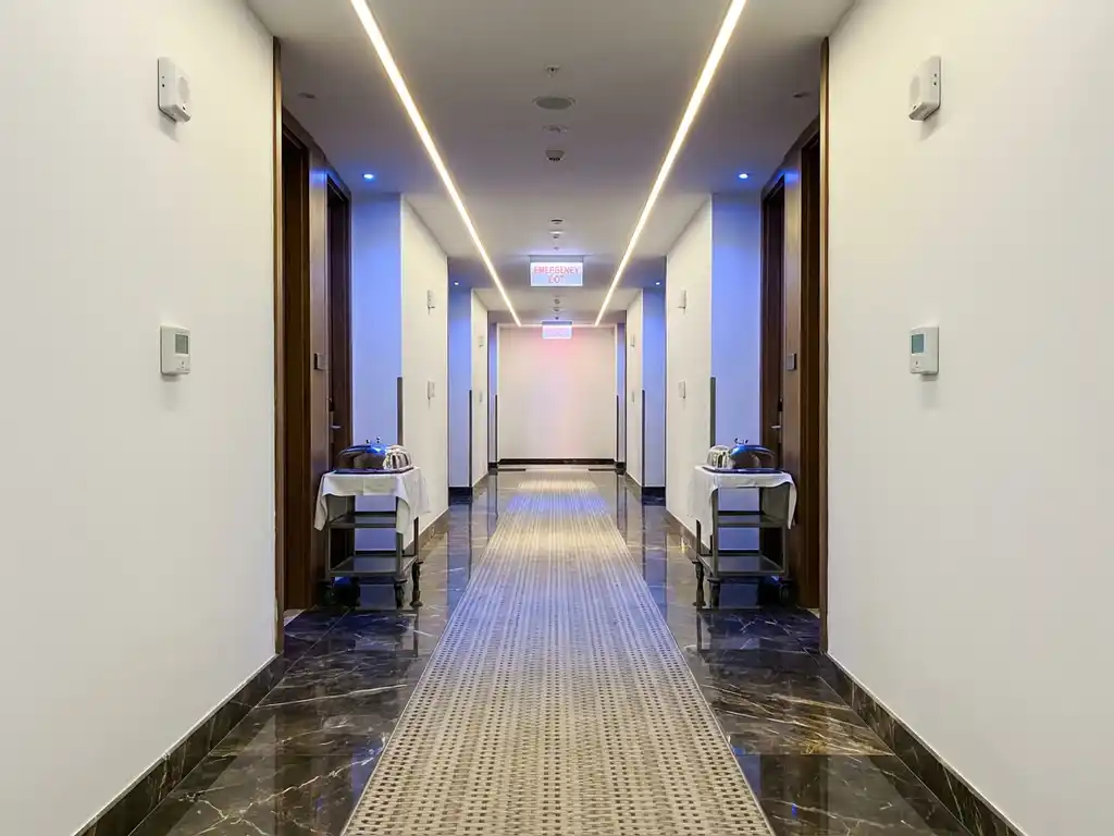 Lege hotelgang met marmeren vloeren, LED-verlichting, veiligheidssensoren aan witte muren en roomservice dienbladen bij gastenkamers