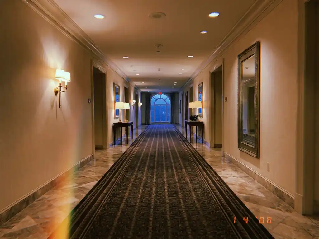 Lege hotelgang met marmeren vloeren, warme plafondverlichting en crèmekleurige muren in avondlicht