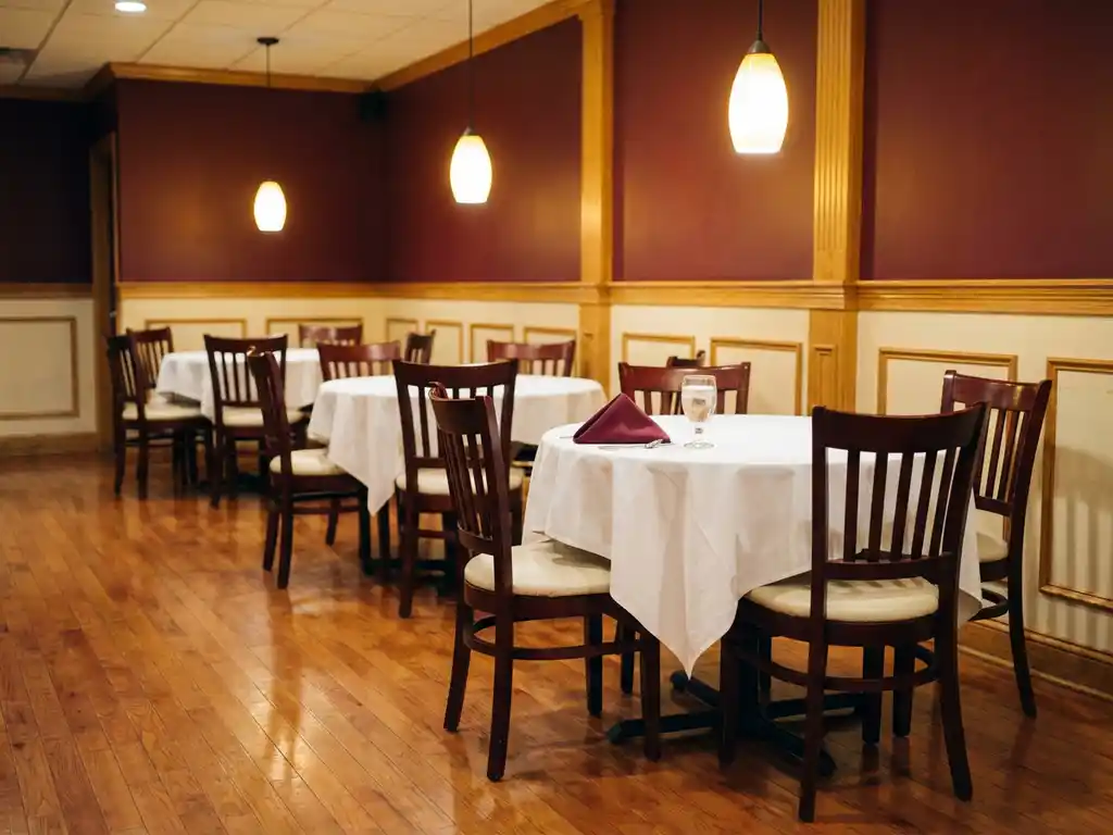 Leeg restaurant met ronde tafels, witte tafelkleden en glanzende hardhouten vloeren onder warme hanglampen