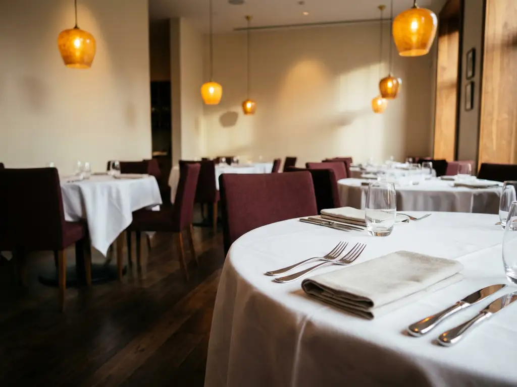 Lege restauranteetaal met gedekte tafels, witte tafelkleden, glanzend bestek en warme hanglampen in burgundy-crème interieur